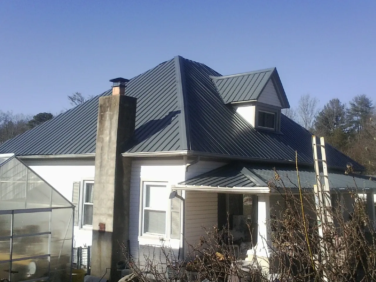 Dark blue standing seam metal roof on a white farmhouse with dormer — Slate & Tile Roof Repair by Roofing Brothers in Fred