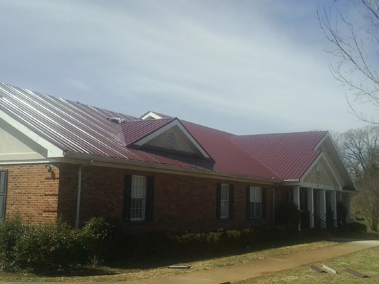 Red metal roof with gabled entries on a long brick building, from a Hail Damage Roof Repair job in Fred
