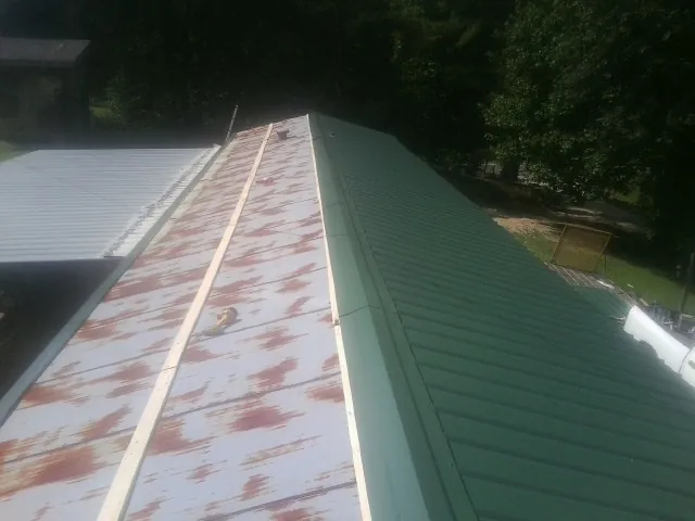 Old rusted panels beside newly installed green metal roofing — Wind Damage Roof Repair by Roofing Brothers in Fred