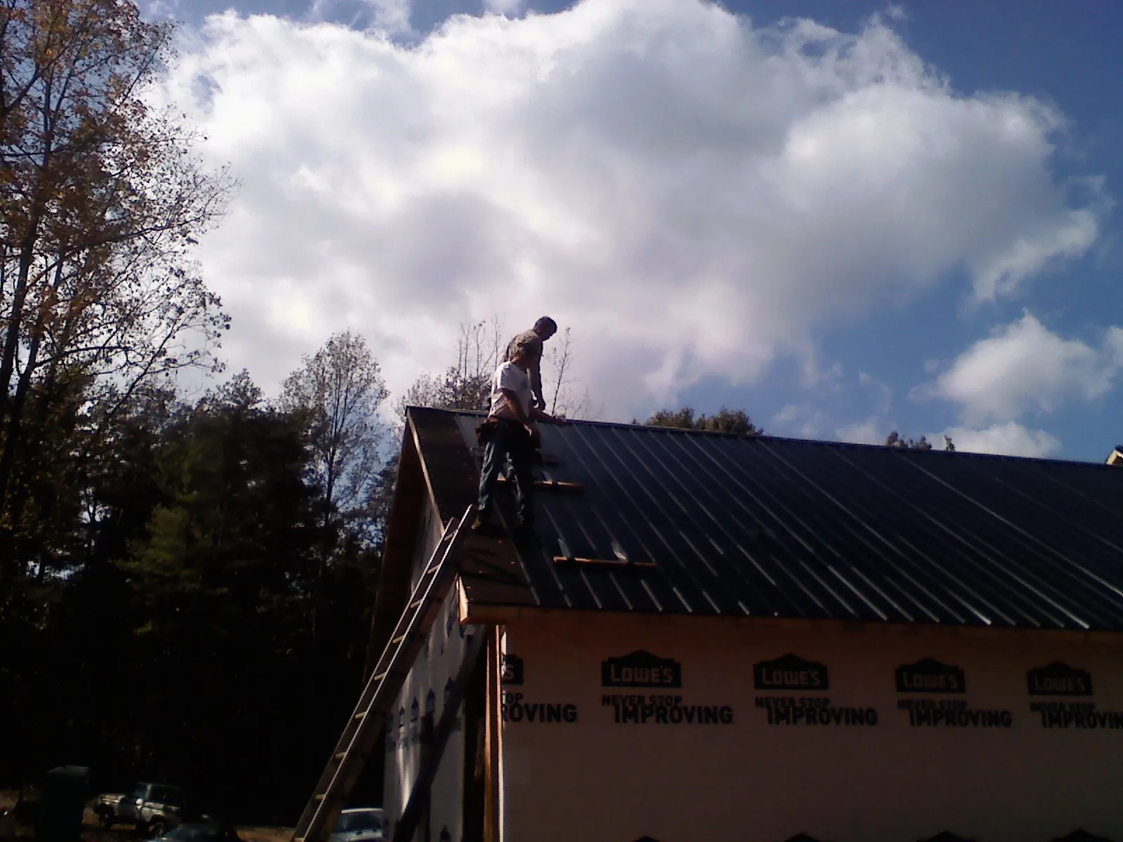 Roofer fastening dark metal panels high against a cloudy sky, from a Roof Inspection job in Fred