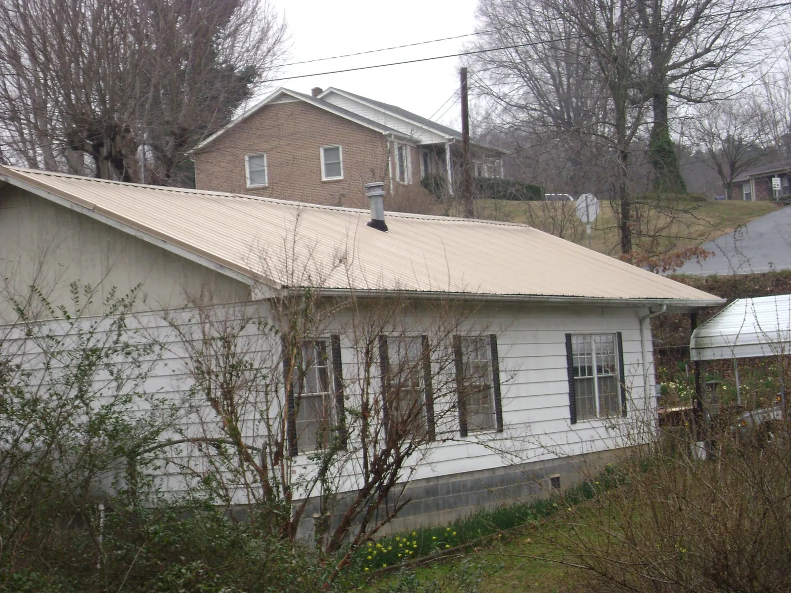 Tan metal roof on a white sided house set into a hillside — Commercial Roofing by Roofing Brothers in Fred